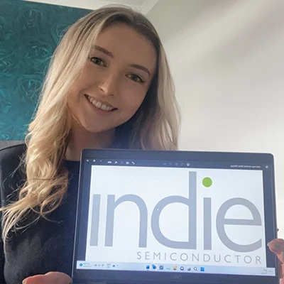 Photo of a woman holding a computer with the indie Semiconductor logo on it.